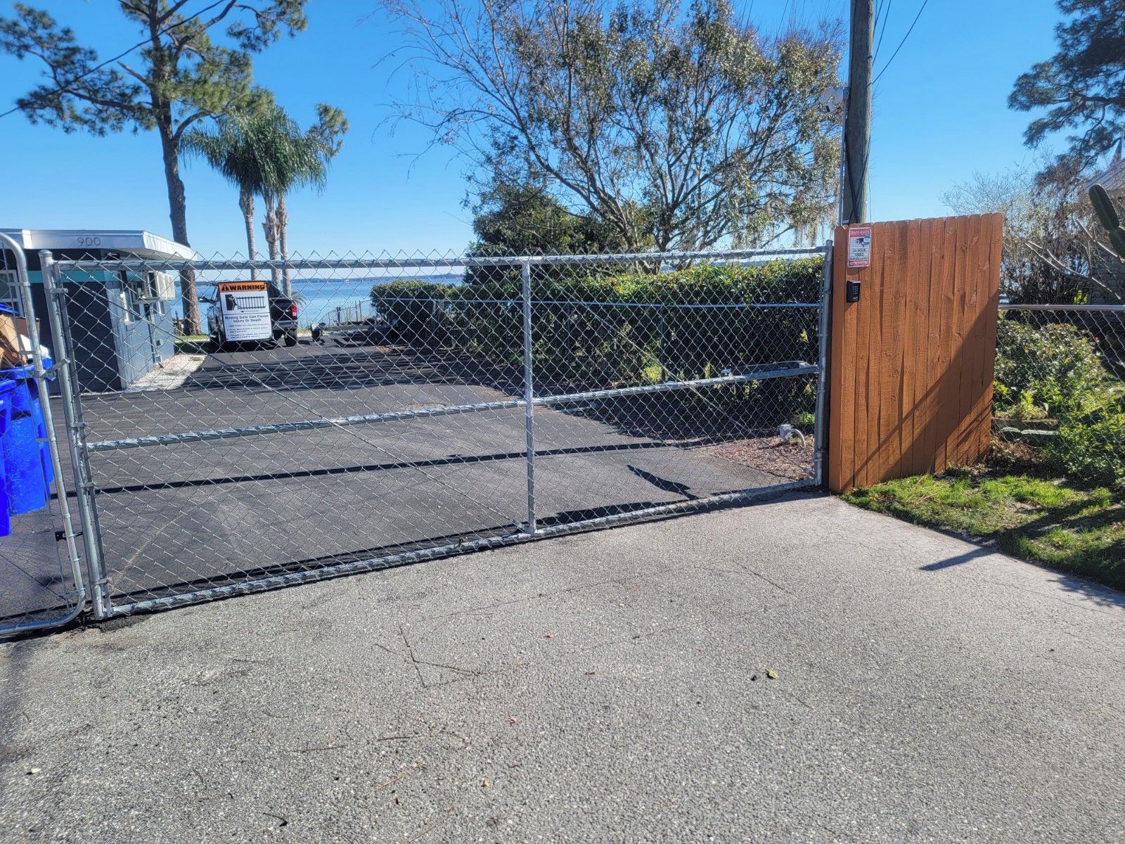 A gated parking area with a chain-link fence, a wooden gate, and a blue dumpster.
