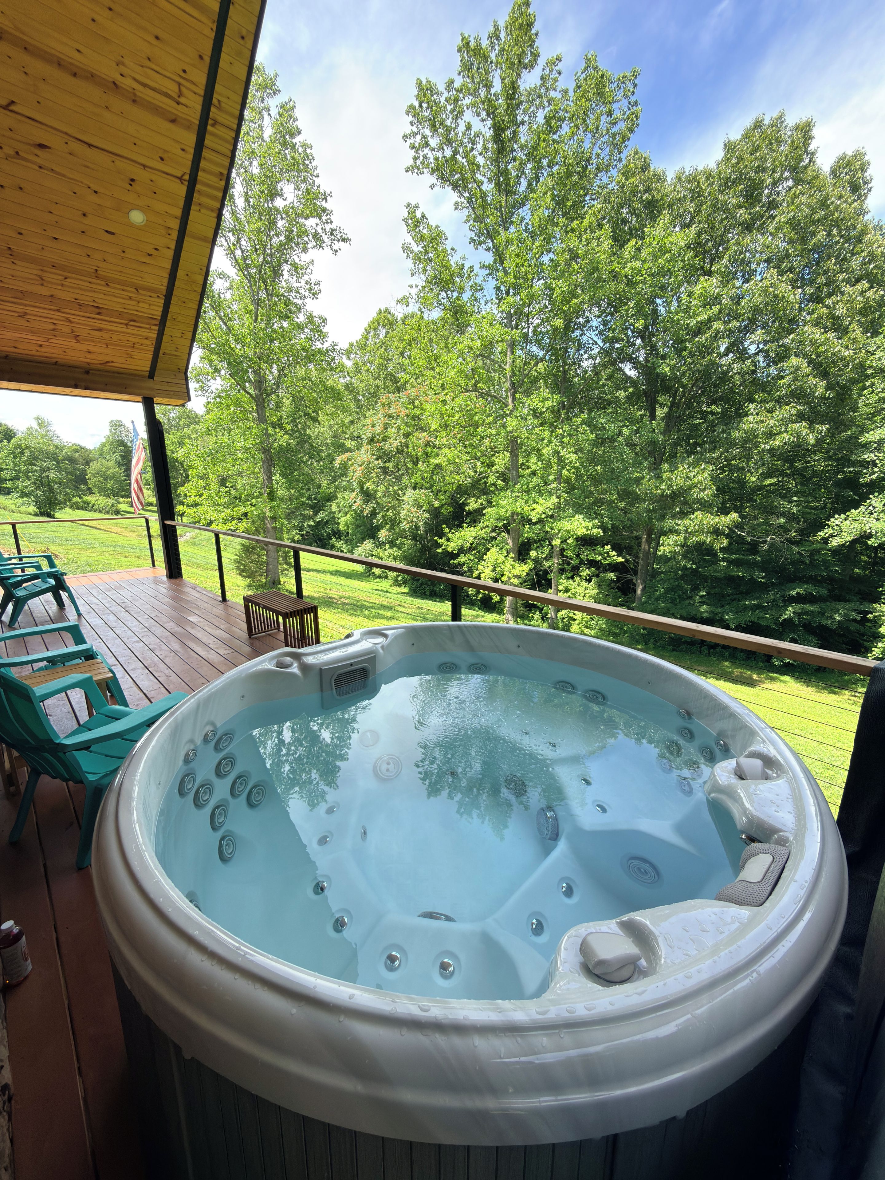 A hot tub on a wooden deck with a view of a grassy area and trees.