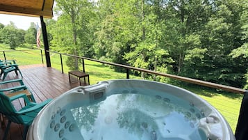A hot tub on a wooden deck with a view of a grassy area and trees.