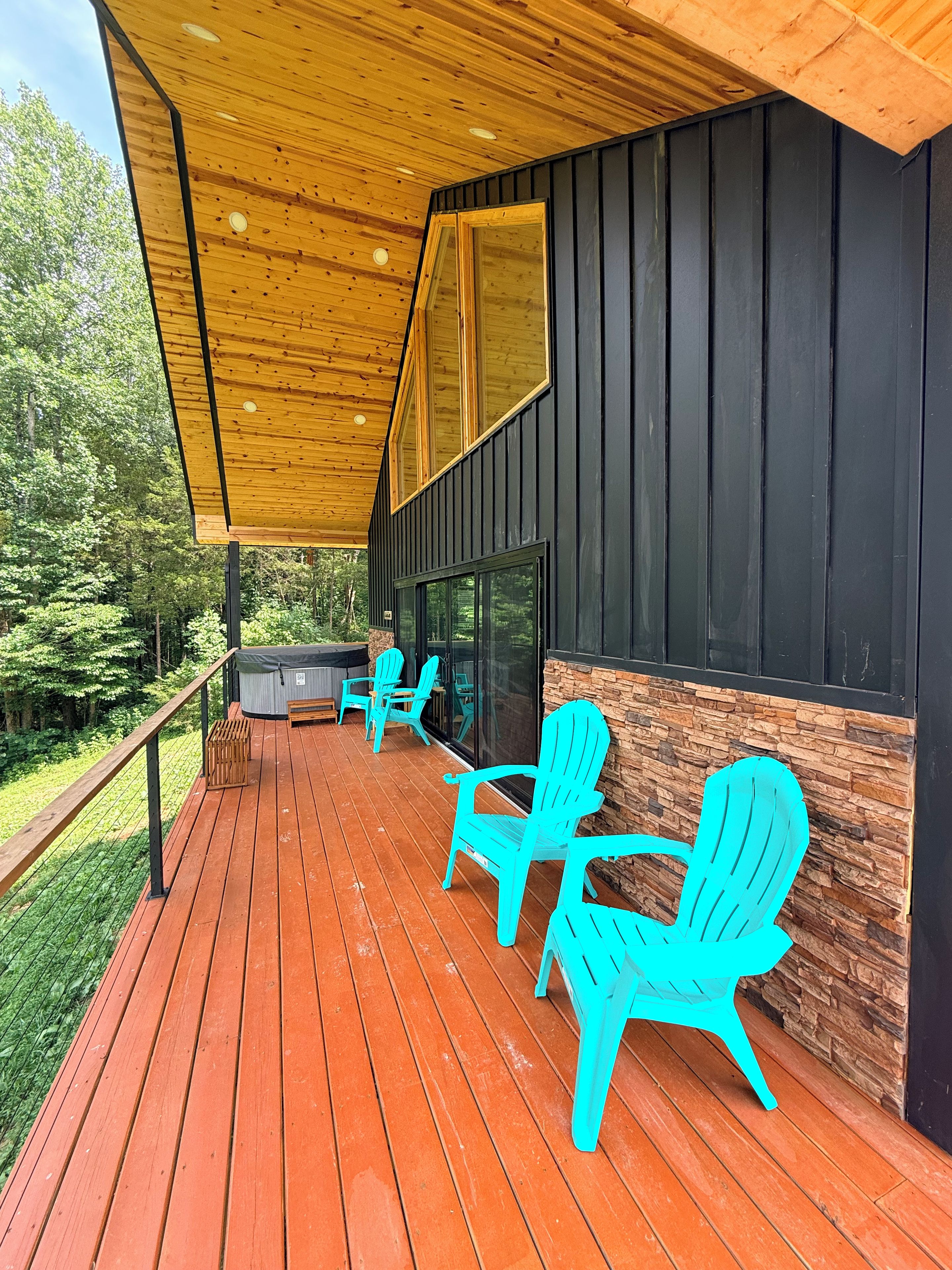 A covered deck with wooden flooring, outdoor seating, and a stone accent wall.