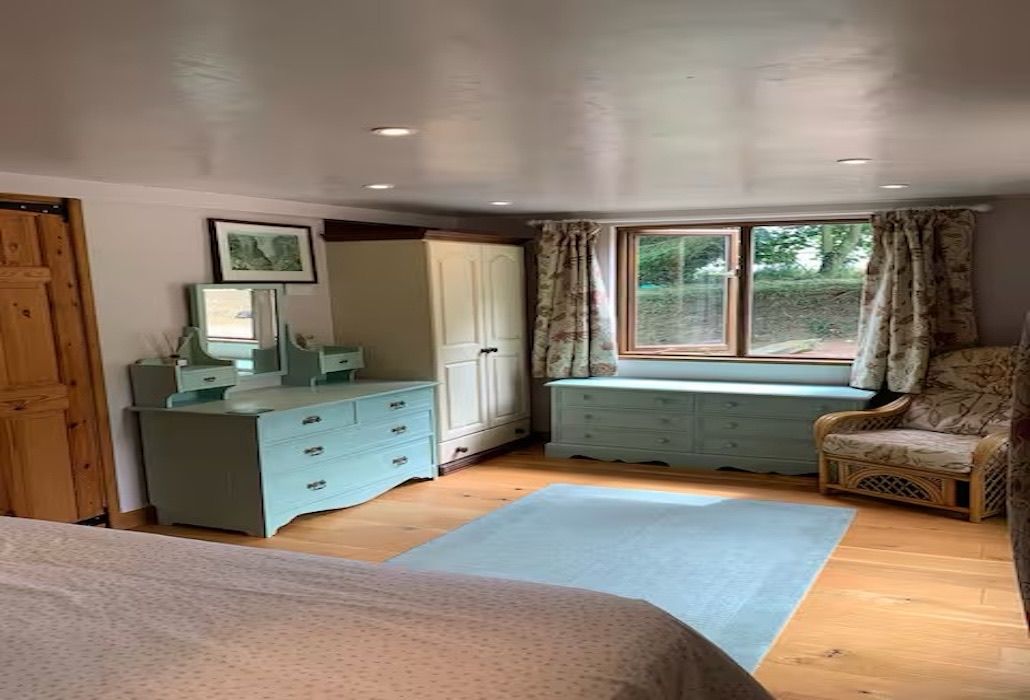 A bedroom with a bed, a dresser, a vanity, a window seat, and a chair.