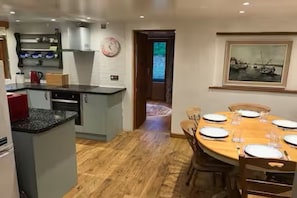 Una cocina moderna con una isla integrada, un área de comedor con mesa de madera preparada para seis personas y un cuadro sobre la mesa.
