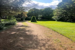 A pathway leading through a park with a well-maintained lawn and dense trees. - Secret, private log cabin in large beautiful  gardens, very quiet, pet allowed (Norwich)