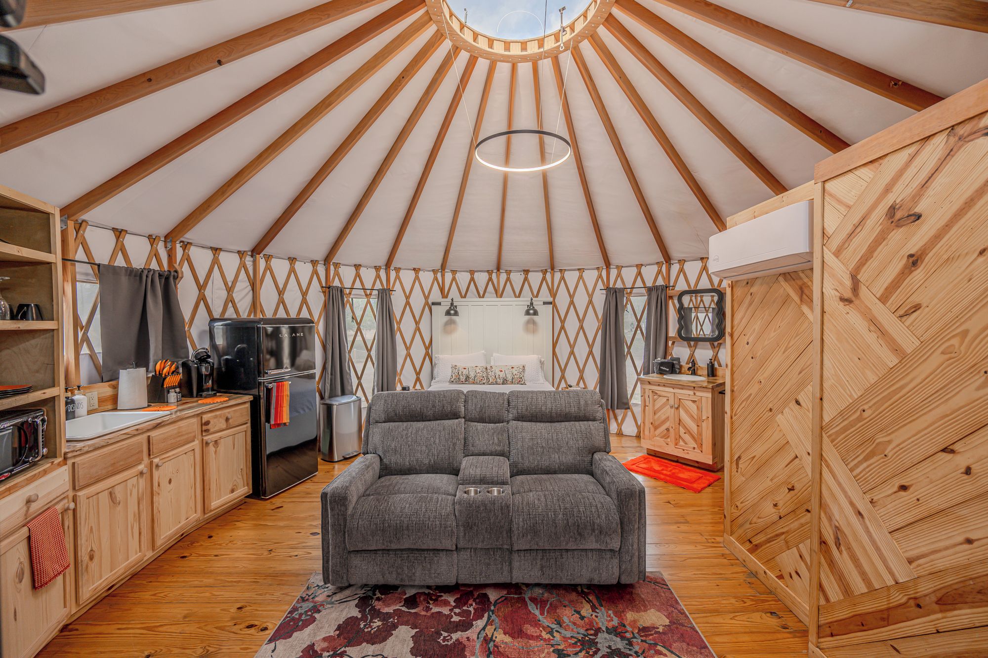 A yurt interior with a sofa, kitchen area, and a hanging light fixture.