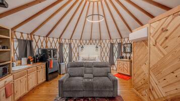 A yurt interior with a sofa, kitchen area, and a hanging light fixture.