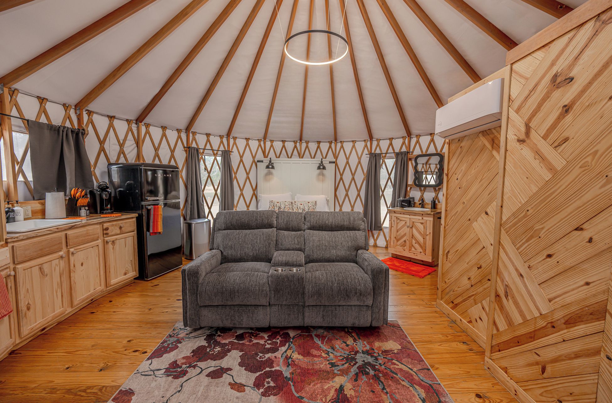 A tented accommodation with a sofa, kitchen area, and wooden walls.