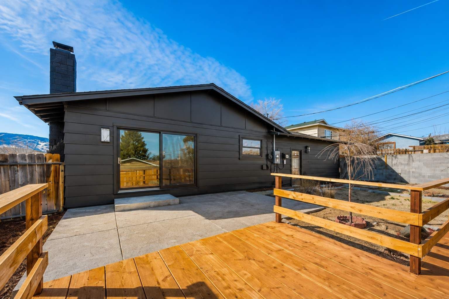 Una casa moderna con un amplio ventanal corredero, una terraza de madera y una cerca de metal.