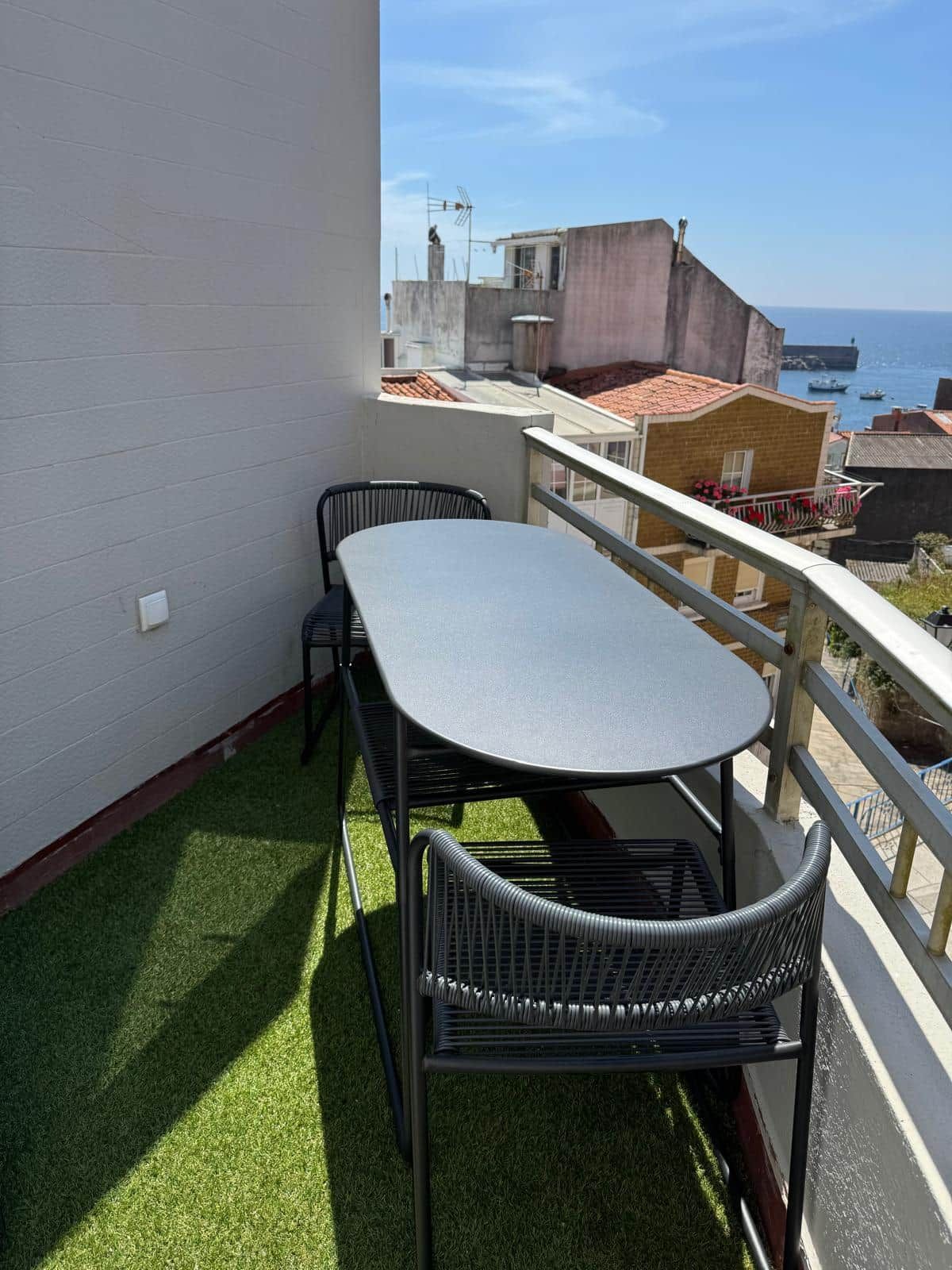 Un balcon avec une table et des chaises, une vue sur la mer et des bâtiments en arrière-plan.