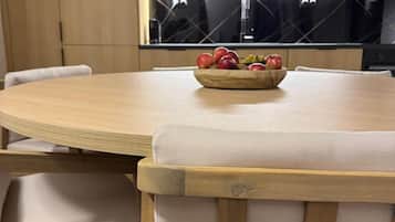 A modern kitchen with a round dining table, wooden chairs, and a bowl of fruit on the table.
