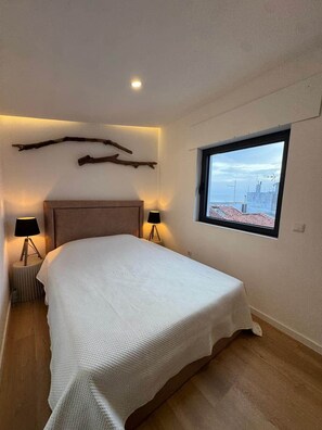 A bedroom with a bed, two bedside lamps, a window with a view, and a wall-mounted light fixture. - La Casita - Aguarda - Pontevedra (A Guarda)