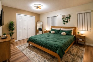 Ein Schlafzimmer mit einem Bett, Nachttischen, einem Spiegel, einem Deckenventilator und einer Wandpflanze.