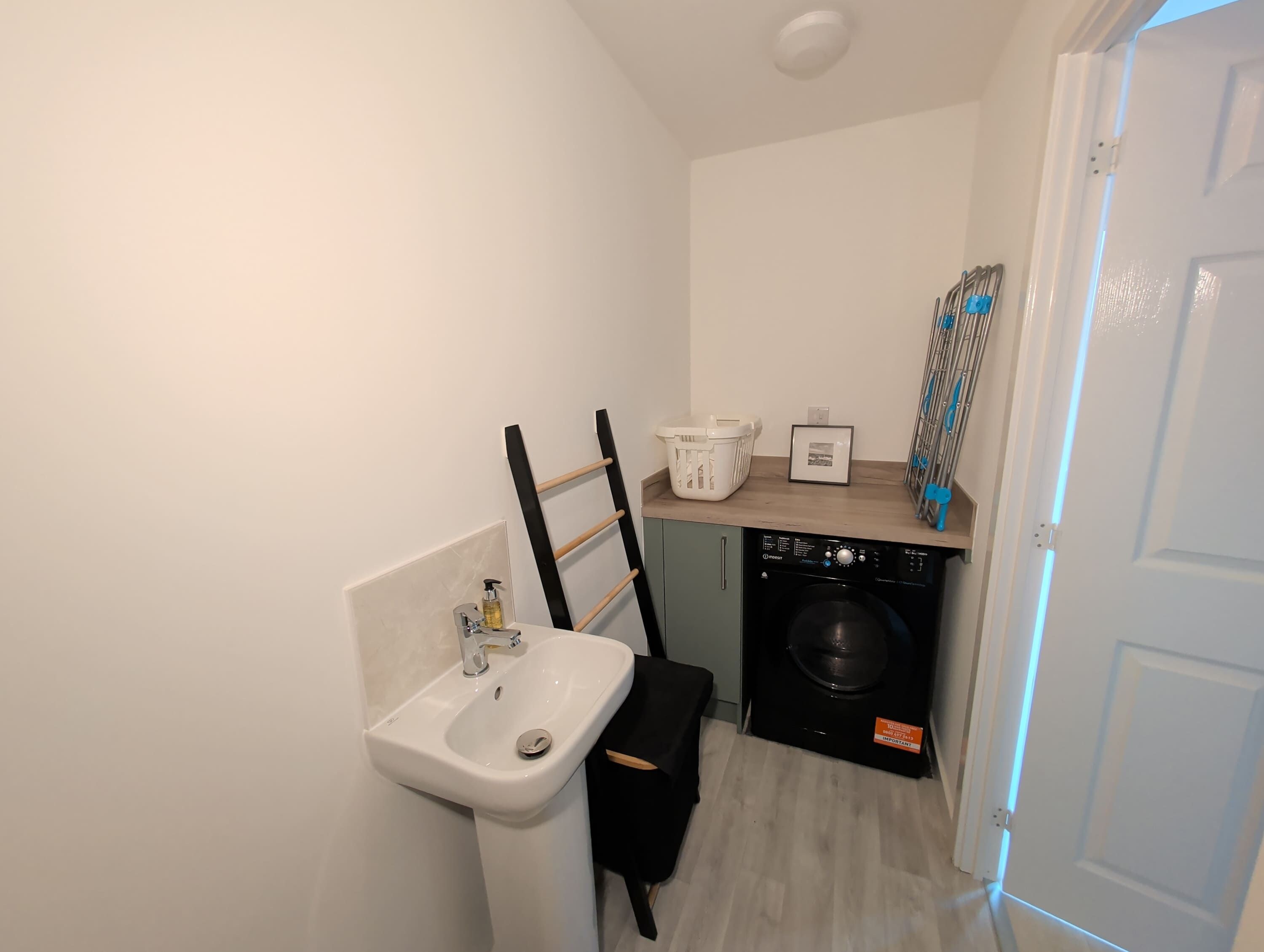 A compact bathroom with a sink, a washing machine, and a drying rack.