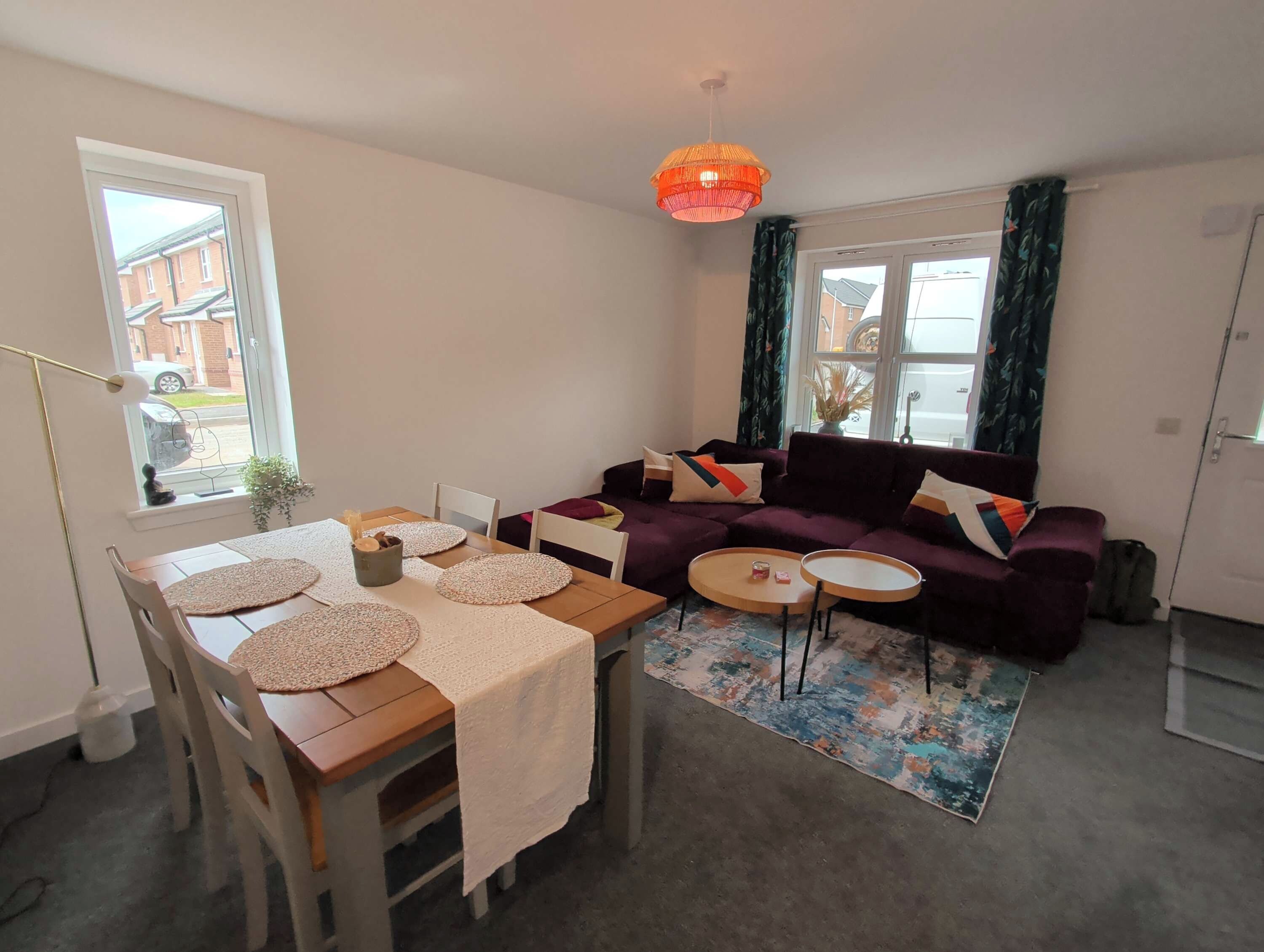 A furnished living room with a sofa, a dining table with placemats, a floor lamp, and a rug.