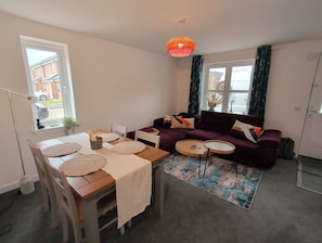 A furnished living room with a sofa, a dining table with placemats, a floor lamp, and a rug. - Stylish 2-Bed Home, Workspaces & Parking (Edinburgh)