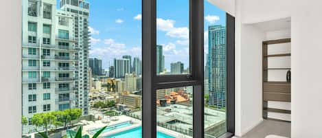 A modern apartment with large windows overlooking a cityscape and a swimming pool.