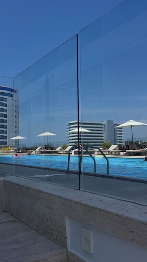 Un área de piscina con sillones de descanso y sombrillas, rodeada de edificios modernos.