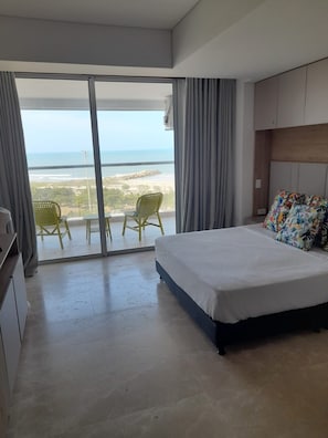 Un dormitorio con cama, escritorio y vista a la playa a través de una puerta corrediza.