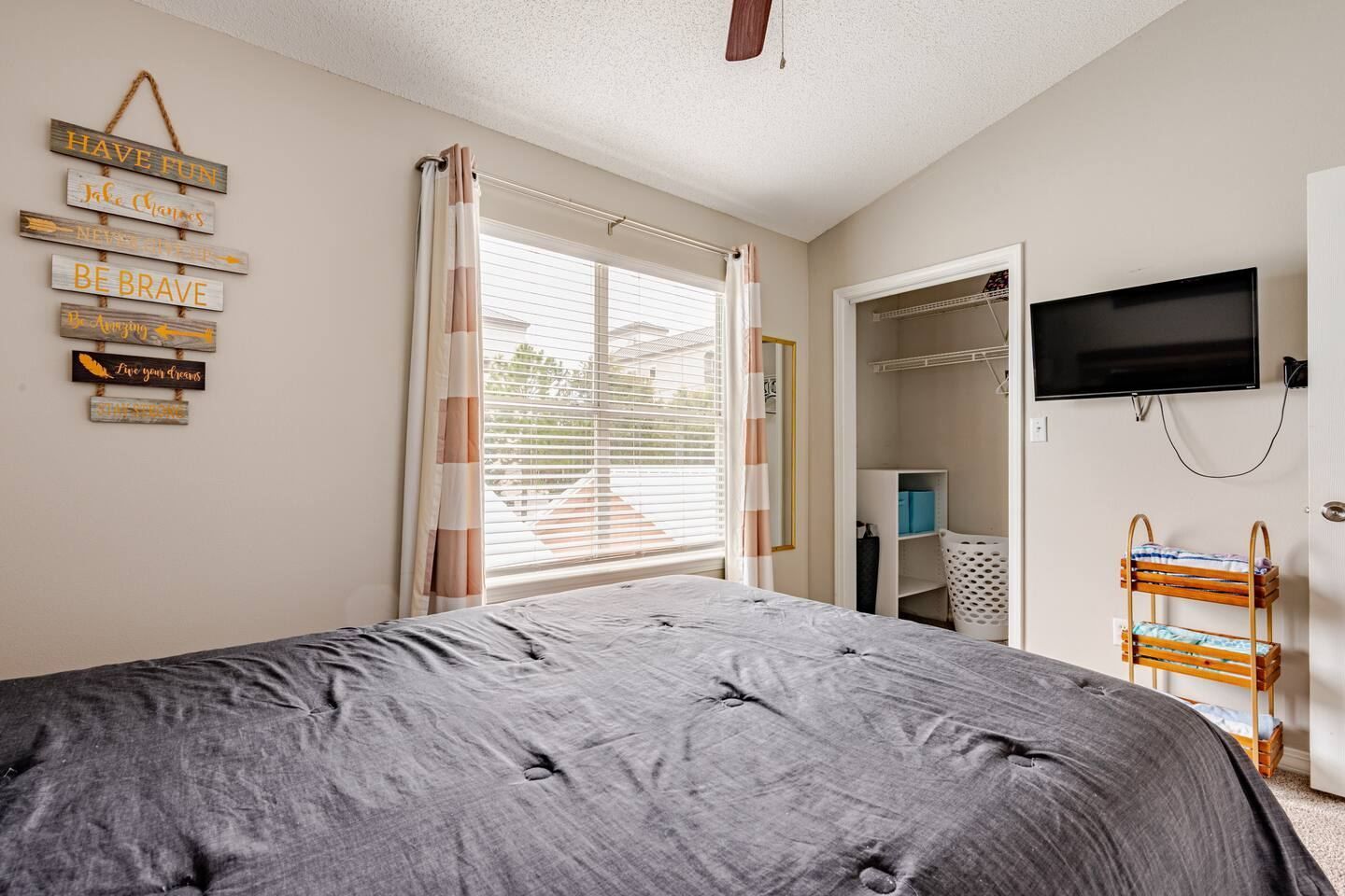 Een slaapkamer met een bed, een aan de muur bevestigde televisie en een raam met zonwering.