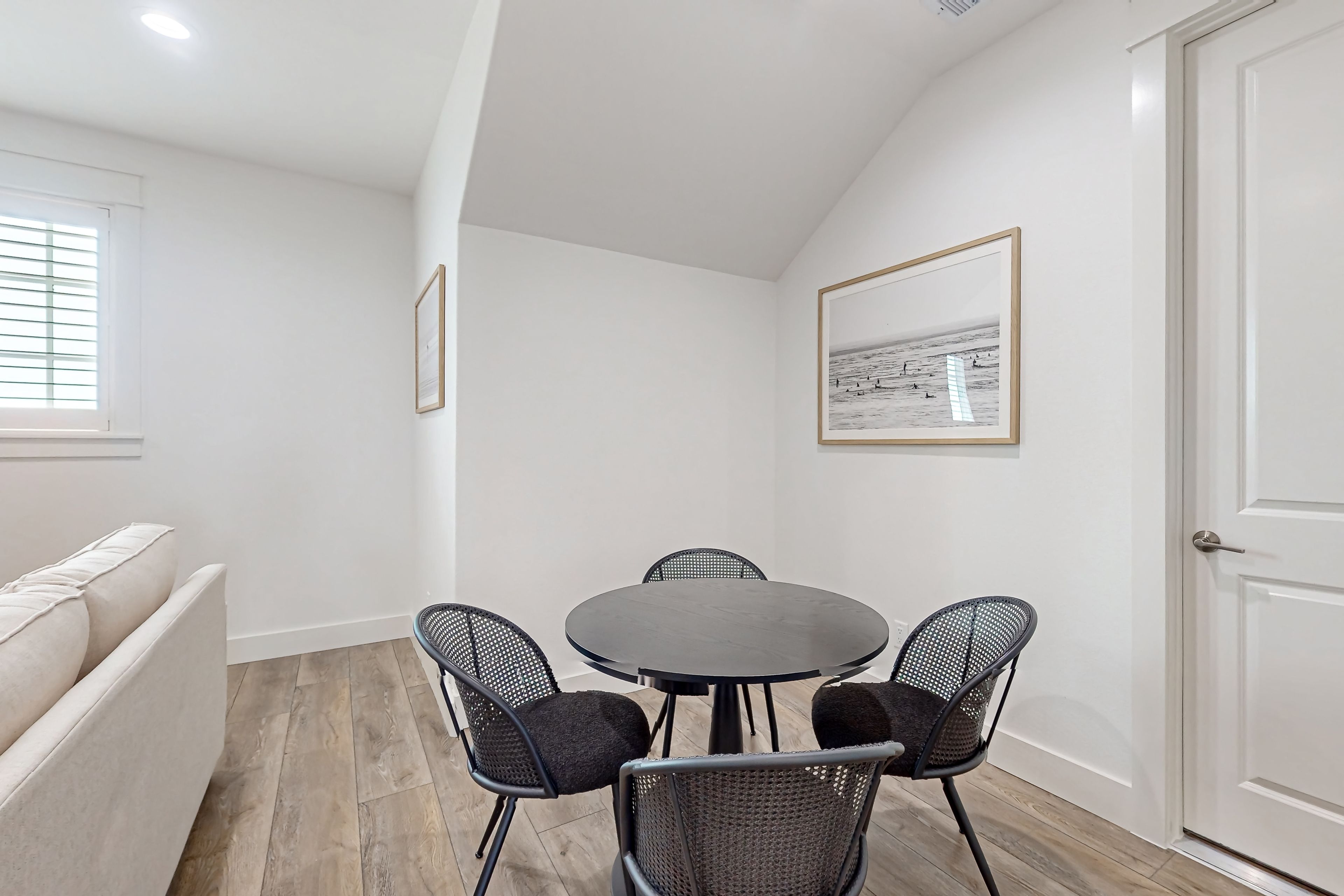 A small, well-lit room with a round table and four chairs, a sofa, and a door.