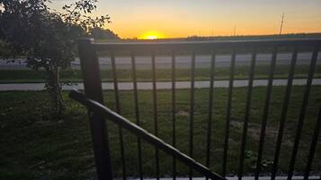 A view of a sunset over a grassy field with a metal fence in the foreground.