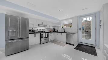A modern kitchen with stainless steel appliances, white cabinetry, and a large window providing natural light.