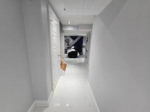 A modern hallway with white walls and a glossy marble floor, leading to a bedroom with a bed and a dresser. - Afterglow Suite | Cozy New| 2 King Bd |10 min Fall (Niagara Falls)