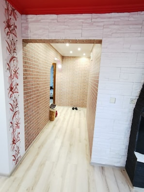 Un couloir avec un mur en briques, un mur blanc recouvert d’un papier peint à motifs floraux et un plancher en bois.