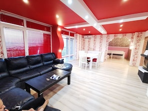 Un salon avec un canapé en cuir noir, une table basse et un coin repas comprenant une table et des chaises blanches.