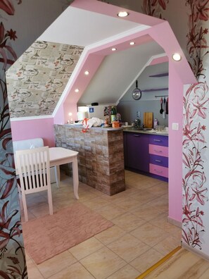 Une cuisine compacte avec un îlot en pierre, un coin repas avec une chaise et un meuble violet.