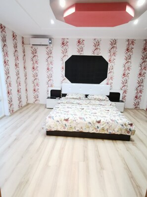 Ein Schlafzimmer mit einem Bett, einem weißen Kopfschild, einer schwarzen Deckenleuchte und floraler Tapete.