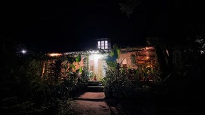 Une maison de nuit, avec une entrée bien éclairée et entourée de végétation.