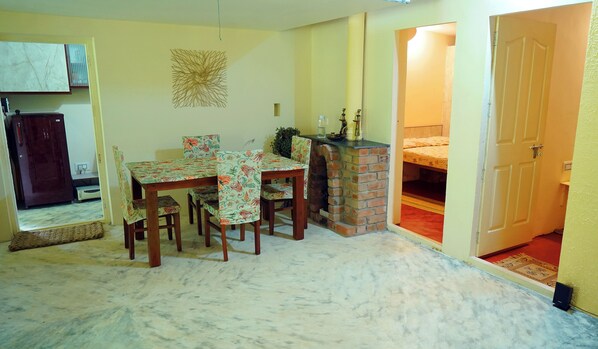 A dining area with a table and chairs, a brick fireplace, and a door leading to another room. - Your Secret Silent Sanctuary.."Tucked in green,Guarded by the Peaks." (Kombankallu)