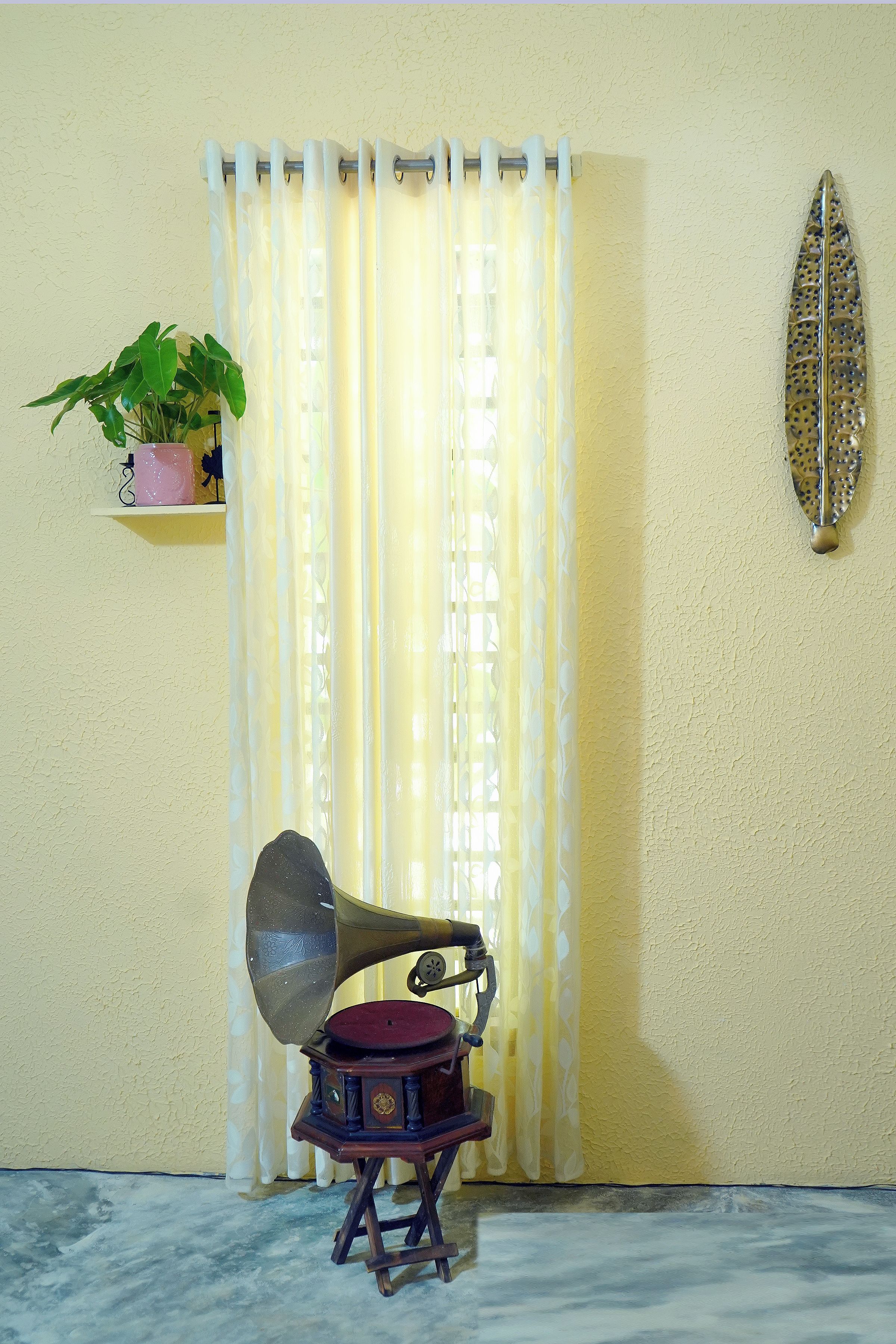 Un vieux gramophone est posé sur une petite table devant une fenêtre ornée de rideaux.