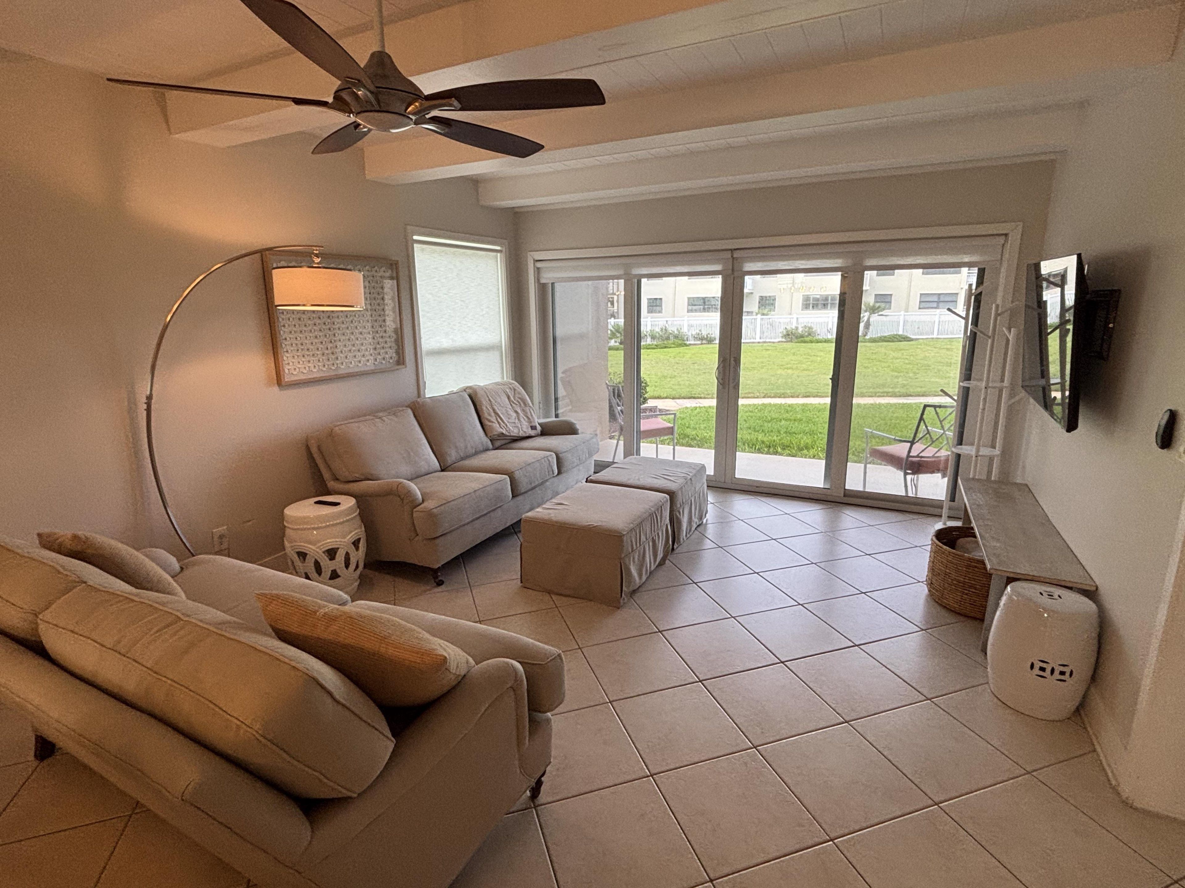 A living room with a sofa, ottoman, and a ceiling fan. There is a sliding glass door leading to a patio.
