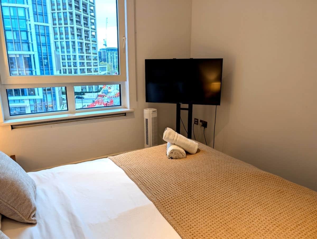 A hotel room with a bed, a TV, a window with a city view, and a towel on the bed.