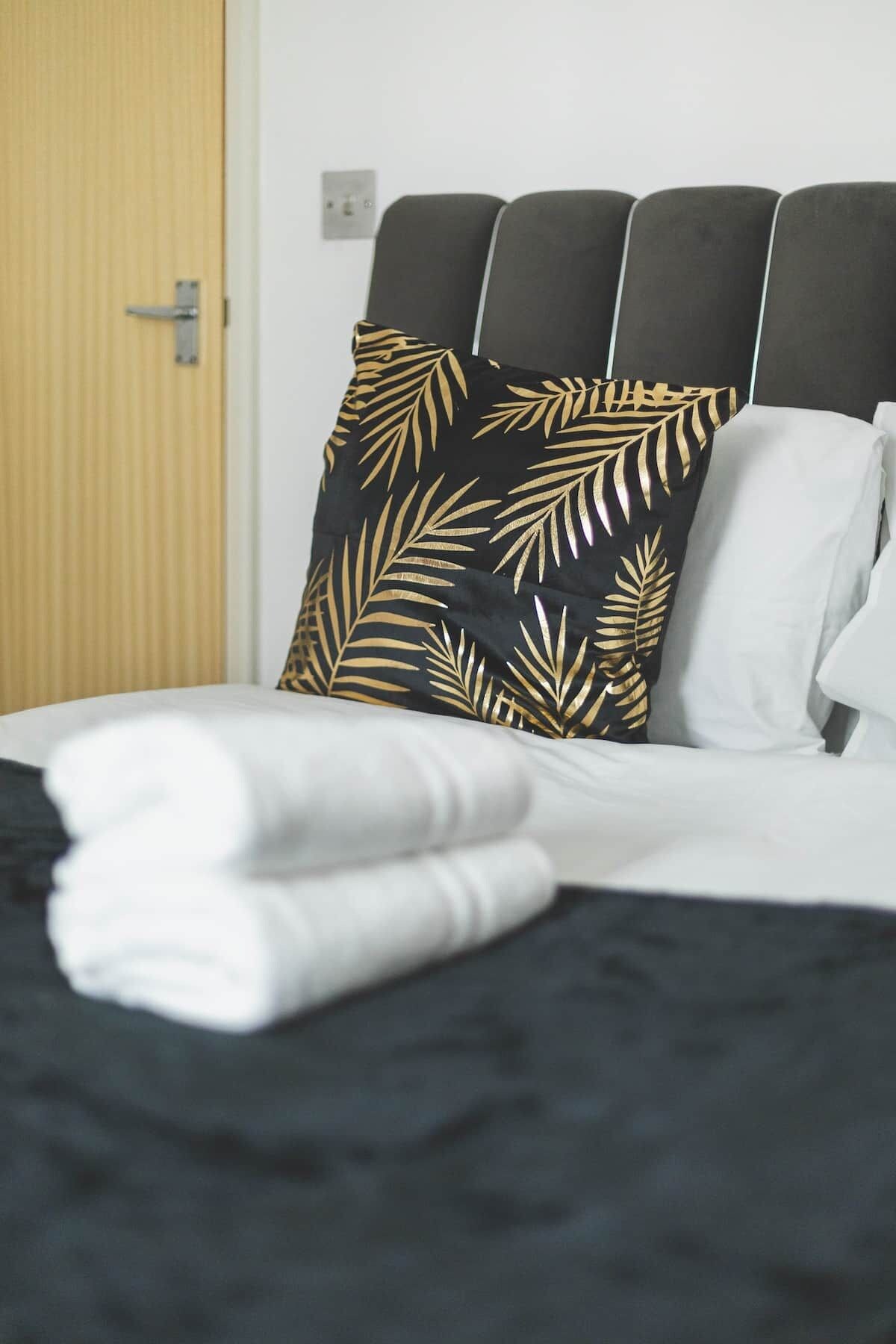 A bed with a black and white bedspread, two pillows with a leaf pattern, and a folded white towel.
