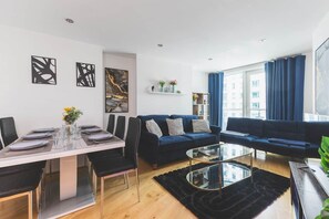 Ett modernt vardagsrum med en matplats, en blå soffa, ett soffbord i glas och konstverk på väggarna.