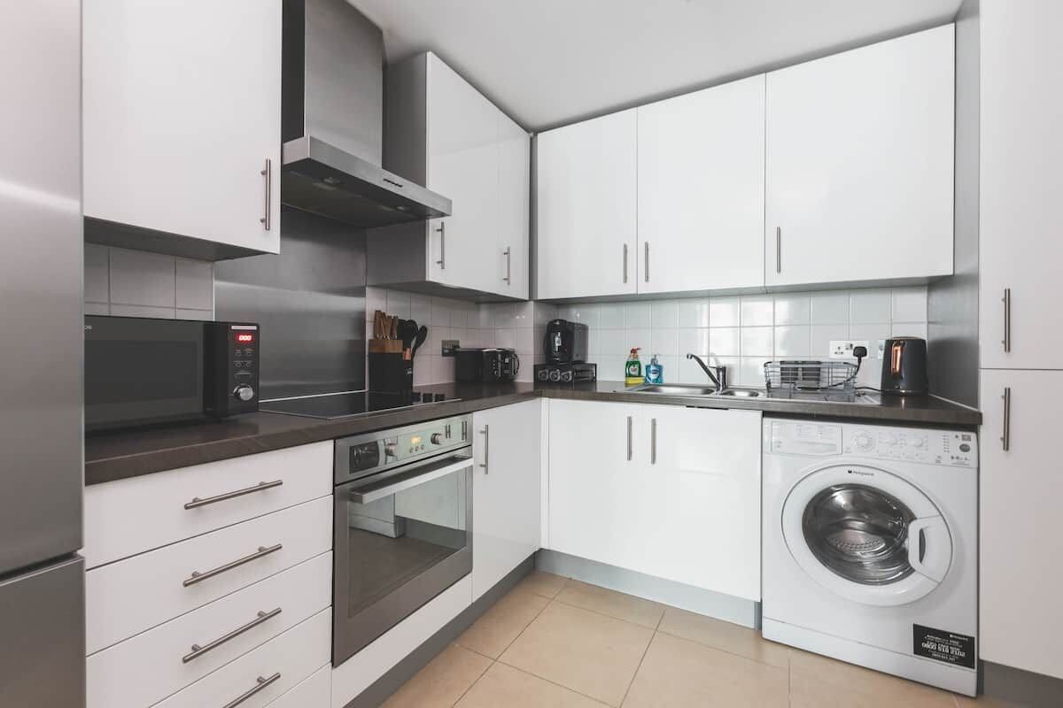 A modern kitchen with white cabinets, a microwave, an oven, a coffee maker, and a washing machine.
