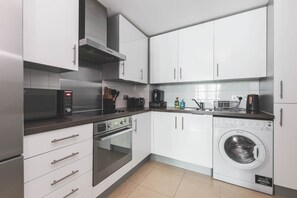 Ett modernt kök med vita skåp, en mikrovågsugn, en ugn, en kaffebryggare och en tvättmaskin.