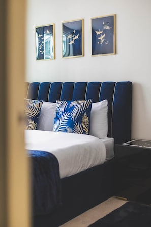 A hotel room with a bed, a bedside table, and three framed artworks on the wall. - Deluxe Two-Bedroom Vauxhall Apartment (London)