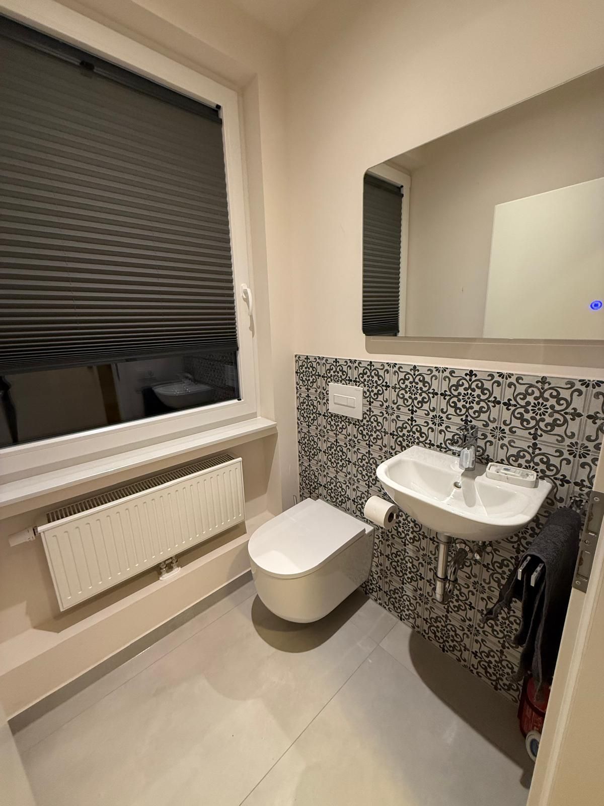 A compact bathroom with a toilet, a sink, and a window with blinds.