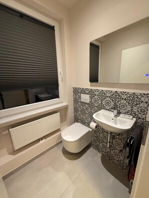 A compact bathroom with a toilet, a sink, and a window with blinds. - New Listing (Essen)