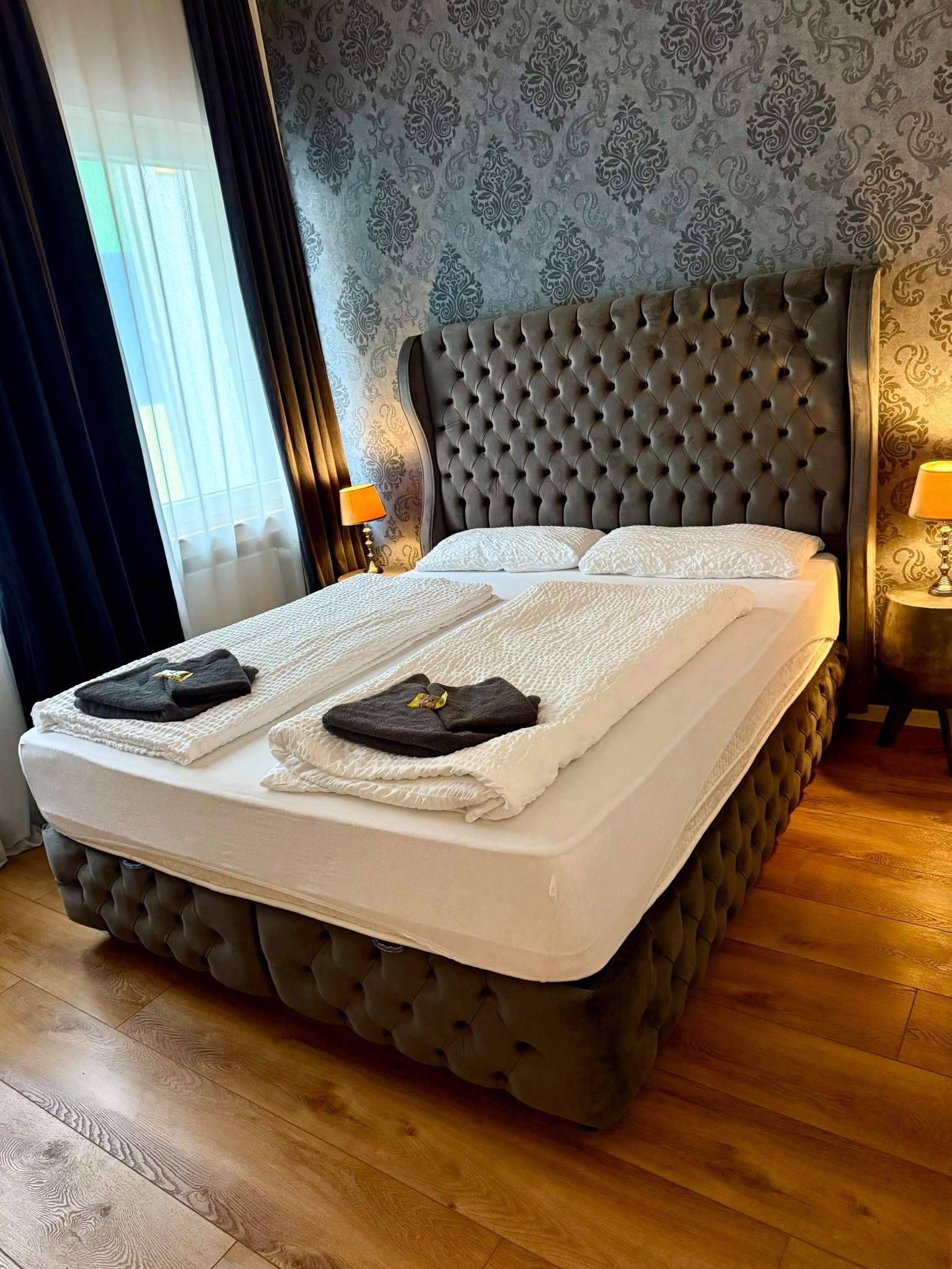 A bed with a tufted headboard, two pillows, and a folded towel on the bed.
