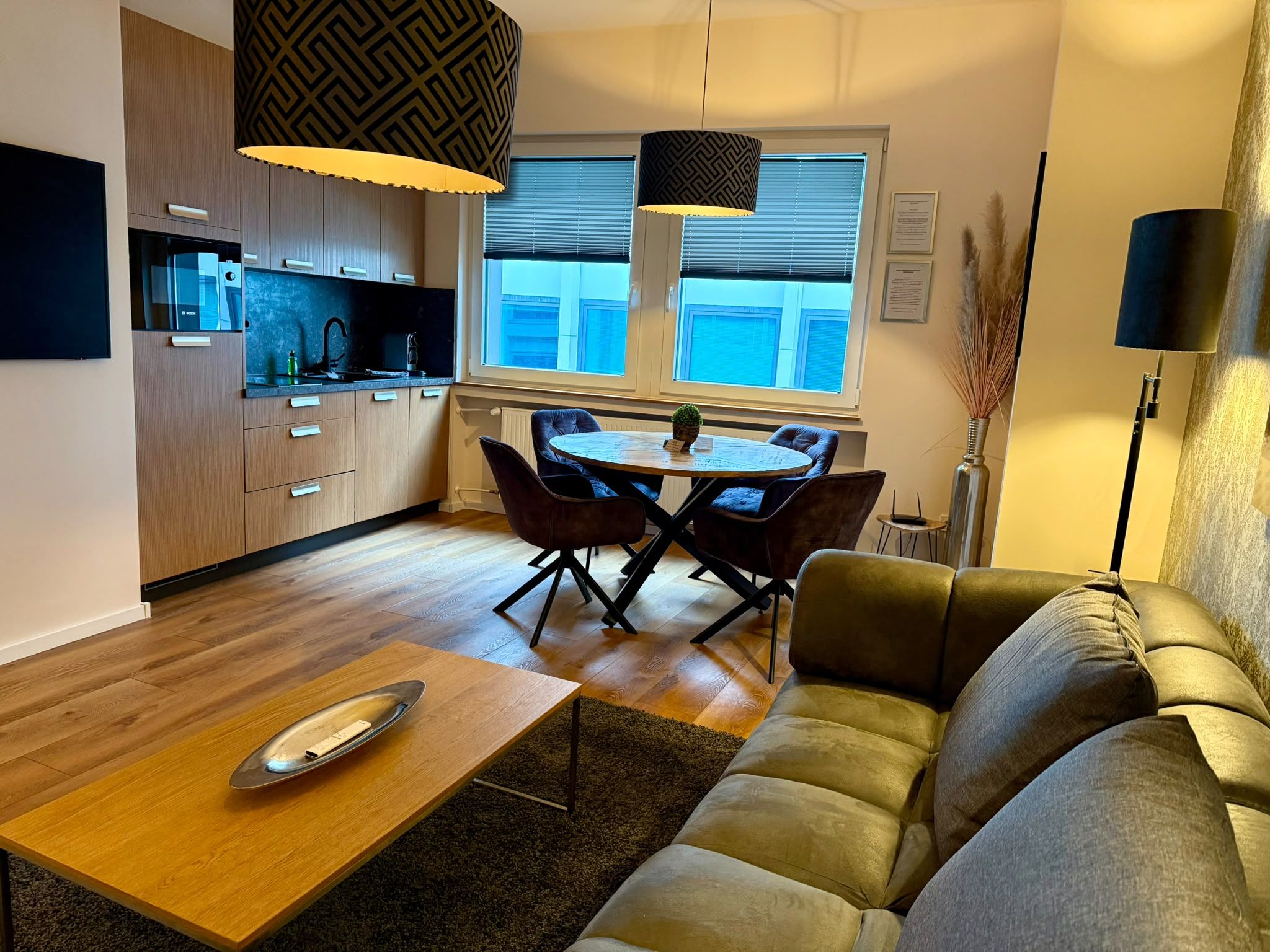 A modern kitchen with wooden cabinets, a dining area with a round table and chairs, and a sofa.