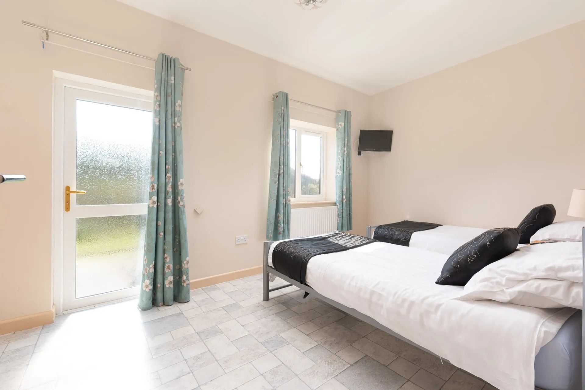 A bedroom with a bed, a television mounted on the wall, and a sliding glass door with curtains.