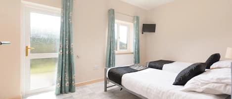 A bedroom with a bed, a television mounted on the wall, and a sliding glass door with curtains.