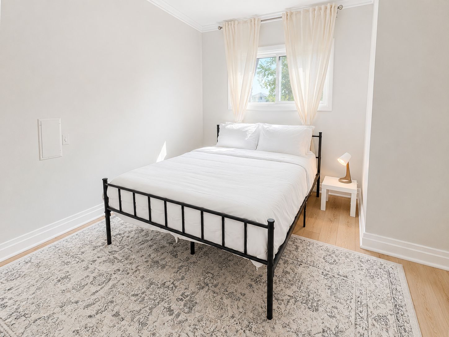 A bedroom with a bed, bedside table, lamp, and a window with curtains.