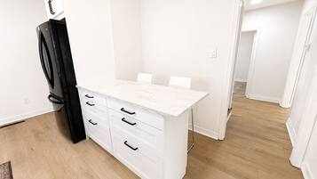 A modern kitchen with white cabinetry, a black refrigerator, and a marble countertop.