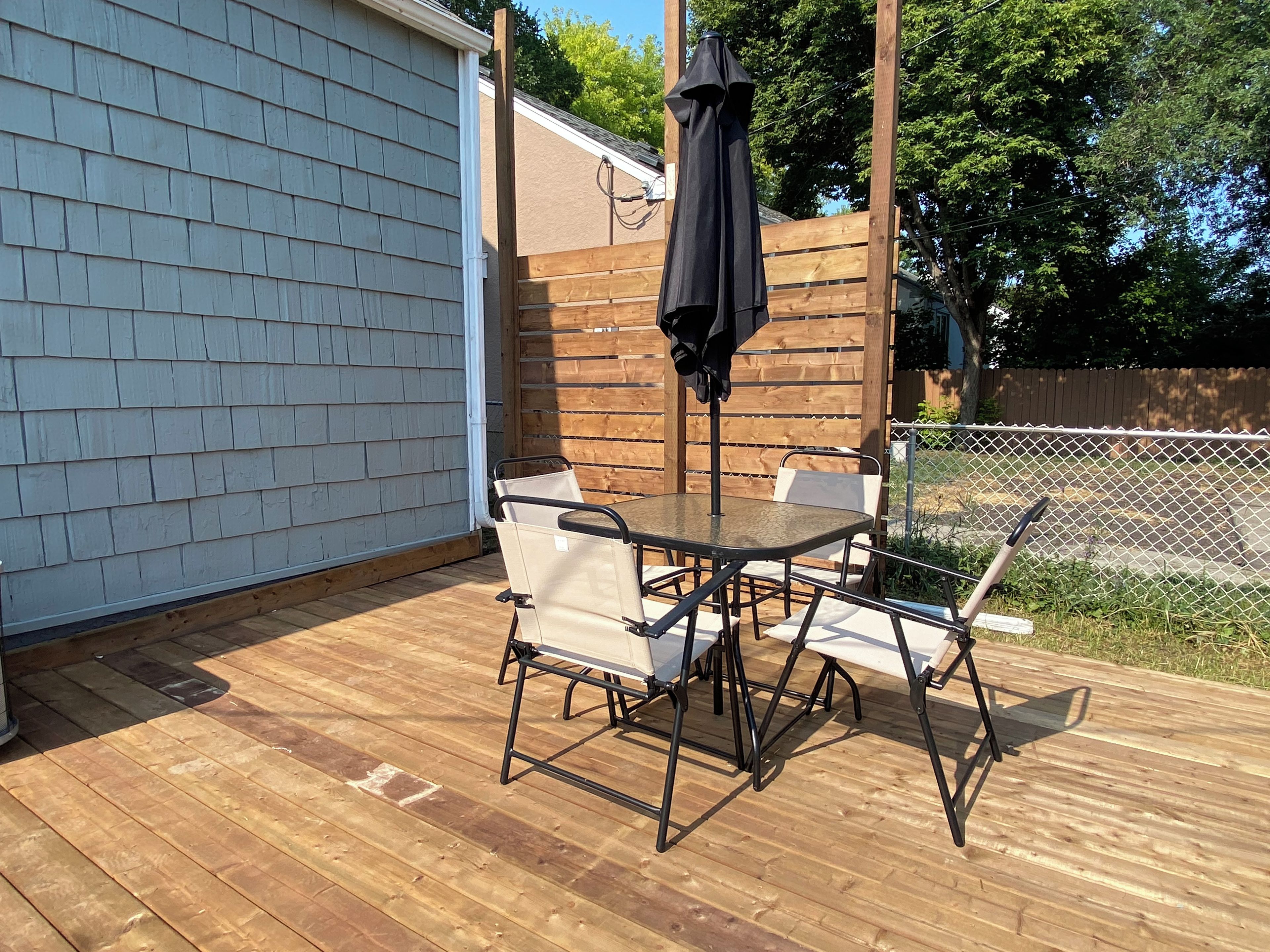 En udendørs terrasse med et bord og stole, et træhegn og en parasol.