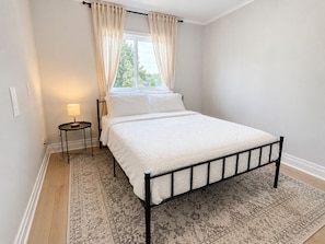 Une chambre à coucher avec un lit, une table de chevet avec une lampe, une fenêtre avec des rideaux et un tapis à motifs.